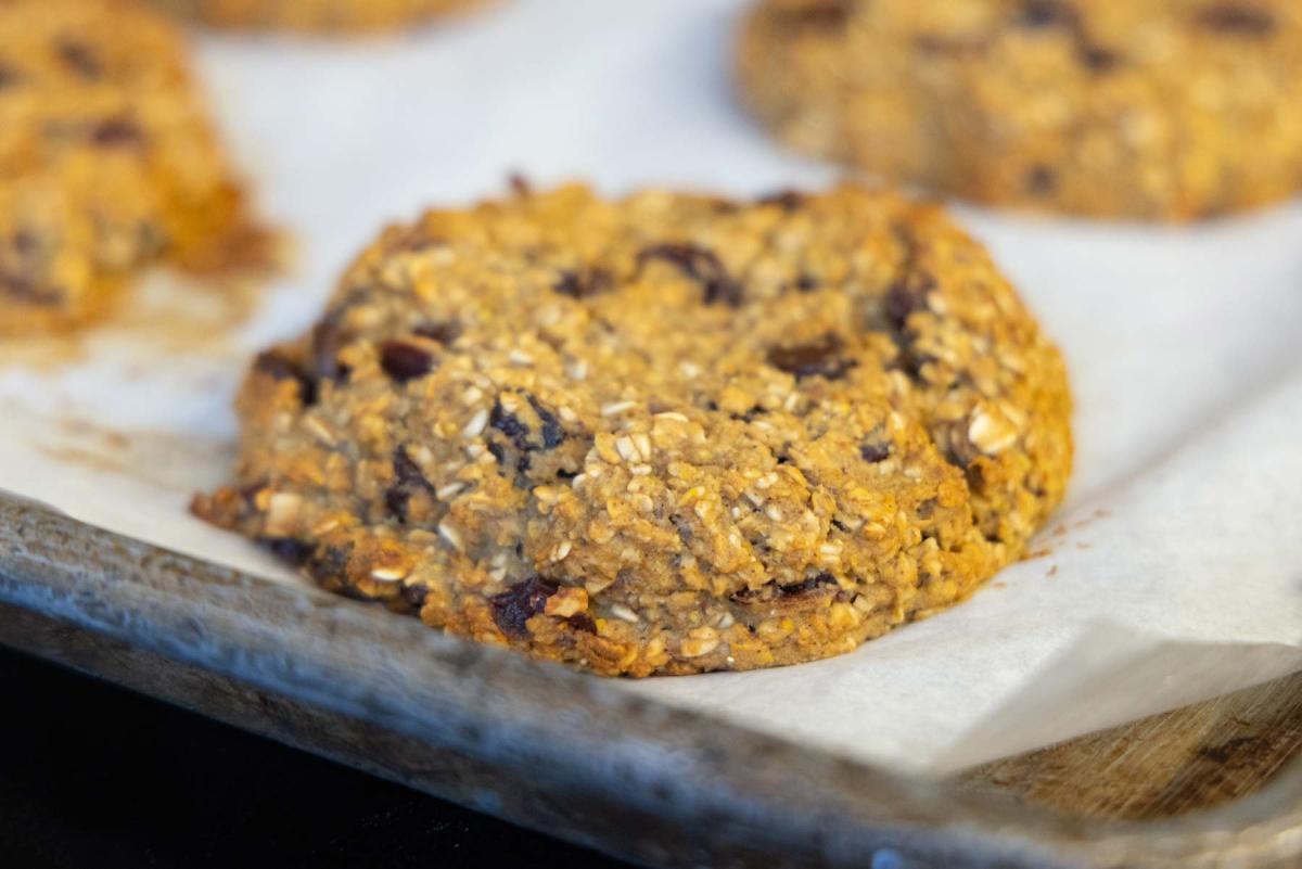 A close-up of a freshly baked oatmeal and raisin cookie resting on a parchment-lined baking sheet. The cookie has a textured surface, speckled with oats and dark raisins. A close-up of a freshly baked oatmeal and raisin cookie resting on a parchment-lined baking sheet. The cookie has a textured surface, speckled with oats and dark raisins.