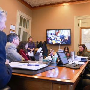 A group of individuals is seated around a large table, engaged in legislative testimony. A group of individuals is seated around a large table, engaged in legislative testimony.