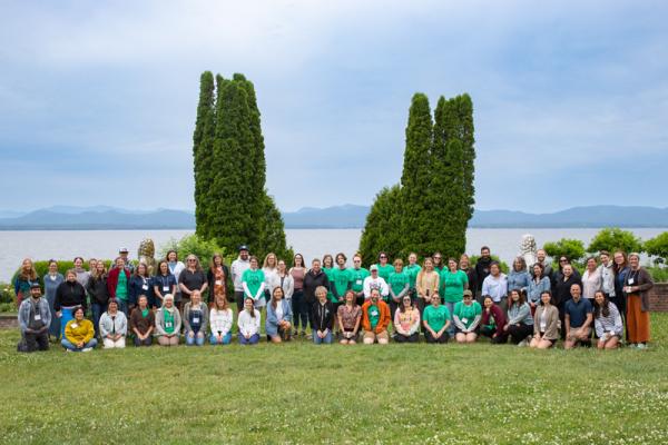 A large group of people gather for a photo, trees, gardens, and a lake in the background. A large group of people gather for a photo, trees, gardens, and a lake in the background.