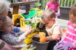 Young learners and an early educator put small squash plants in a pot full of soil