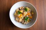 A bowl of wheat berries with roasted squash and parsley garnish, on a wooden table.