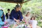 An educator and young kids engage in an outdoor cooking activity in a pavilion.