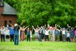 A large group of educators stand outdoors, raising their arms during a movement activity.